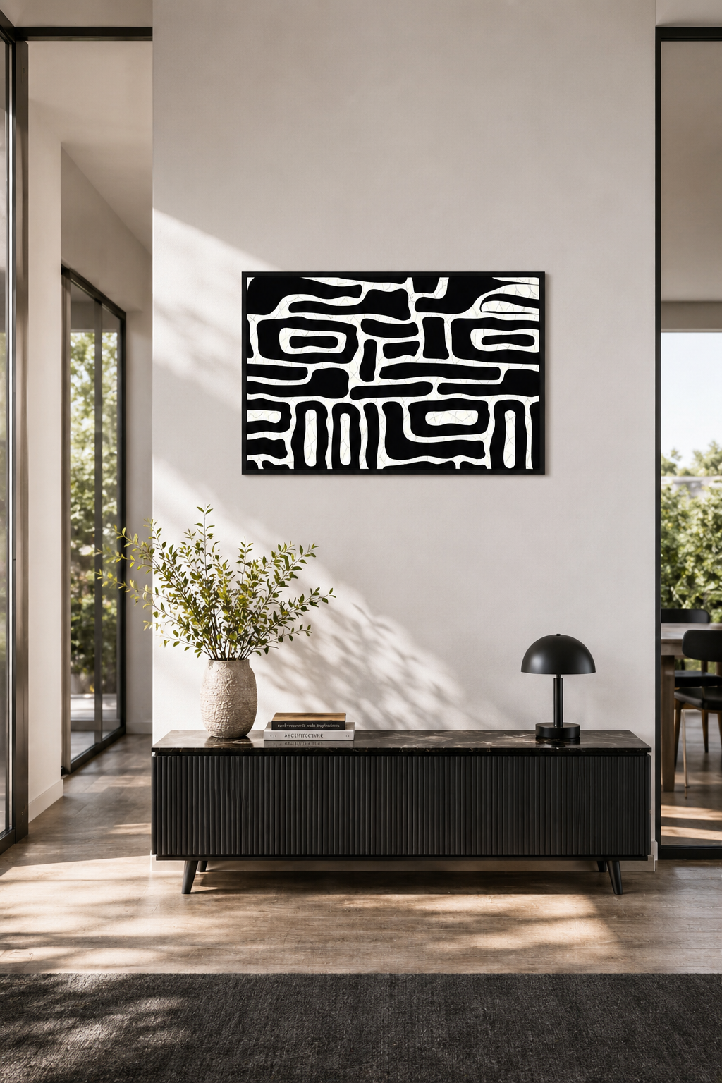 Black and white abstract wall art with a black wooden frame displayed above a modern black console table in a bright entryway with natural daylight and Scandinavian decor.