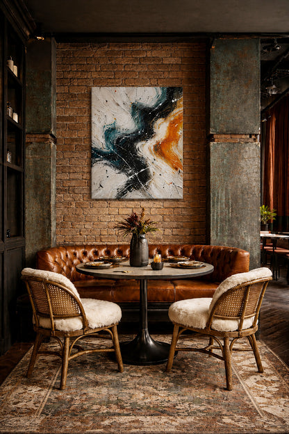 Modern abstract canvas wall art in teal, black and orange tones displayed in a cozy industrial restaurant interior with leather seating and exposed brick wall.