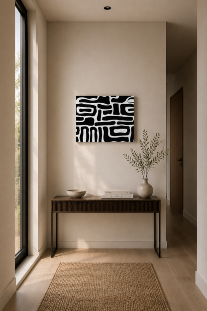 Black and white abstract canvas wall art above a minimalist console table in a bright entryway with natural light