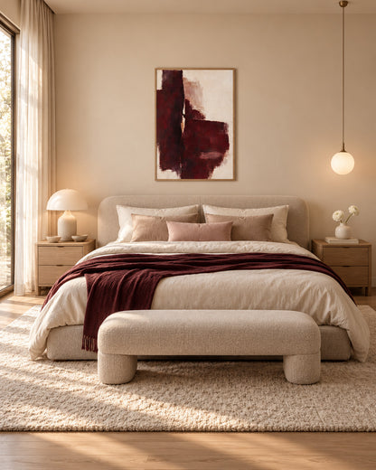 Oxblood Poise burgundy abstract poster in a light wood frame above a cream bed with a burgundy throw